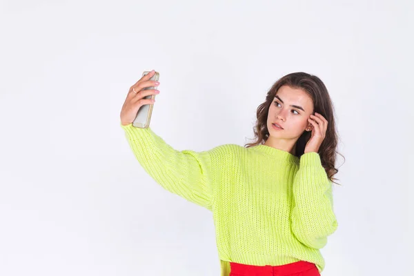 若いです美しいです女性とともにFuckles光化粧でセーター上の白い背景に携帯電話で写真自画撮り — ストック写真