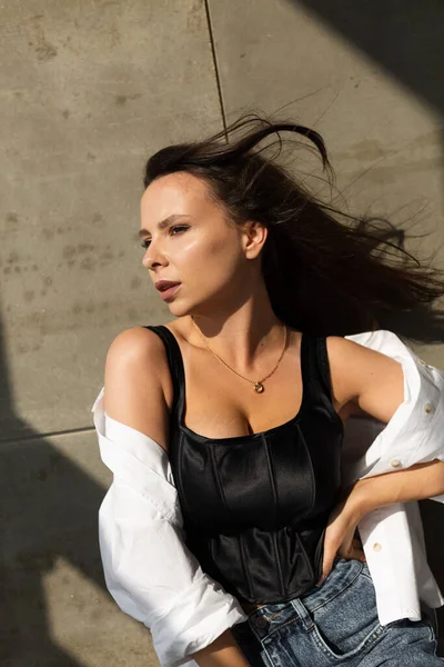 Pretty young woman with big breast posing in studio, by steel wall on background, wearing jeans and white shirt, natural warm sunset light