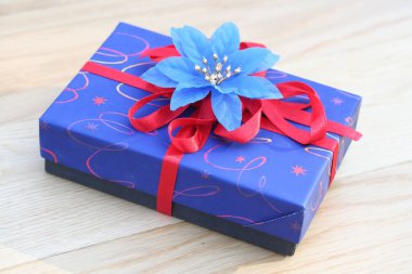 Ahşap arka planda kırmızı kurdeleli mavi Noel hediyesi kutusu