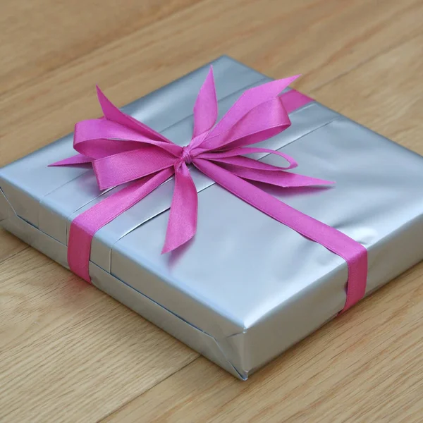木制桌子上有粉色蝴蝶结的银礼品盒 — 图库照片