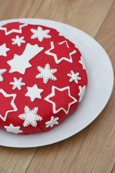 Christmas Cake covered with red sugar paste and white stars on a plate on wooden table