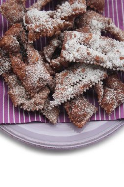 Beyaz arka planda izole edilmiş bir tabakta Crostoli veya Cenci adlı İtalyan Karnaval hamur işleri. Geleneksel çikolatalı Crostoli 