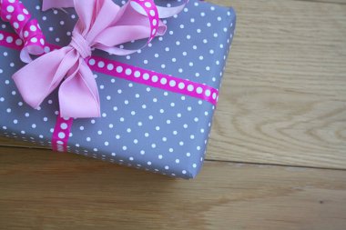 Gri ve beyaz hediye paketi, üzerinde pembe kurdeleler ve ahşap masa