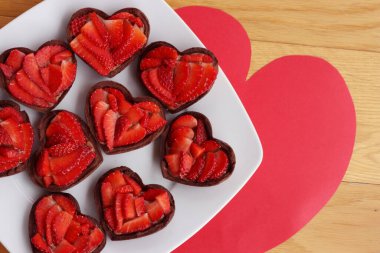 Sevgililer Günü tatlı geçmişi. Minik kalp şeklinde çikolatalı turtalar ve ahşap bir masada taze çilekler.