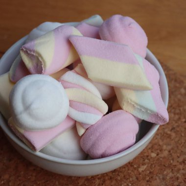 Ahşap bir masada, renkli pembe, beyaz ve sarı şekerlemeler.