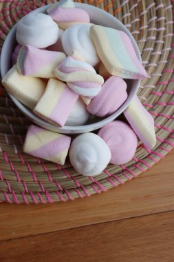 Ahşap bir masada, renkli pembe, beyaz ve sarı şekerlemeler.