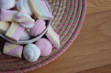 Ahşap bir masada, renkli pembe, beyaz ve sarı şekerlemeler.