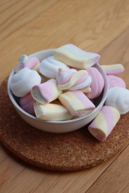 Ahşap bir masada, renkli pembe, beyaz ve sarı şekerlemeler.