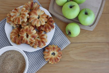 Tarçınlı ev yapımı puf elma halkaları ve beyaz seramik tabakta kamış şekeri tahta masada taze elmalarla birlikte.