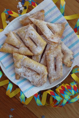 İtalyan tatlısı, kızarmış hamur tatlısı ve ahşap masaya şeker serpiştirilmiş. Chiacchere veya crostoli, bugie, rengarenk konfeti ve kağıt yılanbalığıyla cenci
