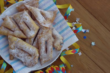 İtalyan tatlısı, kızarmış hamur tatlısı ve ahşap masaya şeker serpiştirilmiş. Chiacchere veya crostoli, bugie, rengarenk konfeti ve kağıt yılanbalığıyla cenci