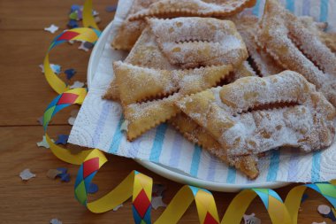 İtalyan tatlısı, kızarmış hamur tatlısı ve ahşap masaya şeker serpiştirilmiş. Chiacchere veya crostoli, bugie, rengarenk konfeti ve kağıt yılanbalığıyla cenci