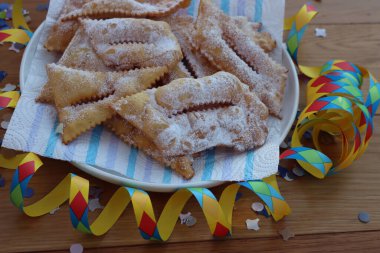 İtalyan tatlısı, kızarmış hamur tatlısı ve ahşap masaya şeker serpiştirilmiş. Chiacchere veya crostoli, bugie, rengarenk konfeti ve kağıt yılanbalığıyla cenci
