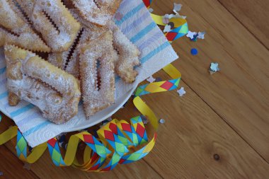 İtalyan tatlısı, kızarmış hamur tatlısı ve ahşap masaya şeker serpiştirilmiş. Chiacchere veya crostoli, bugie, rengarenk konfeti ve kağıt yılanbalığıyla cenci
