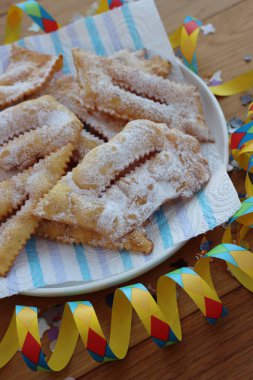 İtalyan tatlısı, kızarmış hamur tatlısı ve ahşap masaya şeker serpiştirilmiş. Chiacchere veya crostoli, bugie, rengarenk konfeti ve kağıt yılanbalığıyla cenci