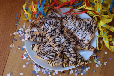 İtalyan usulü çıtır kraker, bol yağda kızartılmış ve ahşap masaya koyu çikolata serpiştirilmiş. Chiacchere veya crostoli, bugie, konfeti ve kağıt şeritli cenci