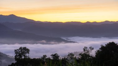 Sabah sisi ormanlık tepelerin üzerinde süzülür altın ışık uzak dağ zirvelerinin ardında parlarken.
