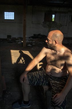 Model bir adam terk edilmiş bir deponun karanlık boşluğunda oturuyor. Gölgesi yerde yatıyor. Yaşamın geçiciliğini ve şu anı düşünüyor..