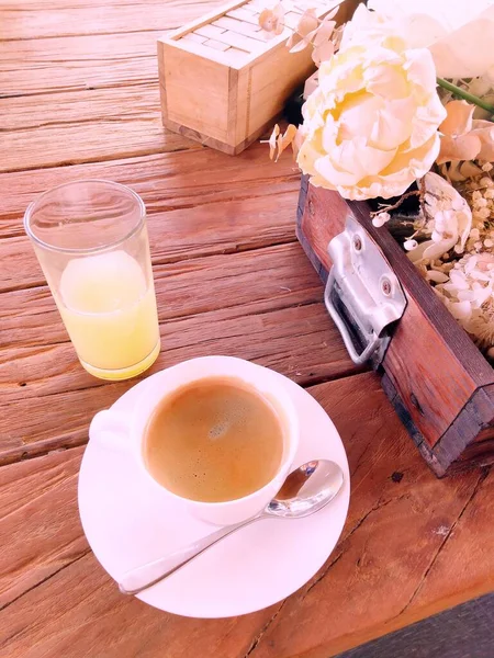 Beyaz fincanda sıcak espresso ve portakal suyu ahşap bir masaya konur..