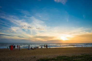 İnsanlar sahilde günbatımı okyanus üzerinde seyrediyor.