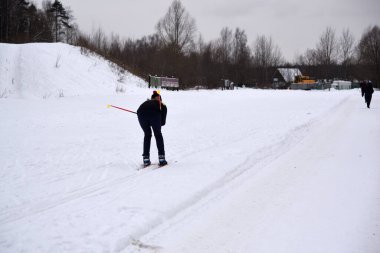 Kış mevsiminde bir kayakçı şehrin varoşlarındaki ormanda kar altında spor kıyafetleriyle kayak yapıyor.