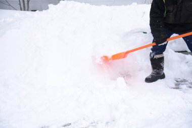 Bir işçi kaldırımlardan kar kaldırır turuncu bir kürekle sürüklenir.