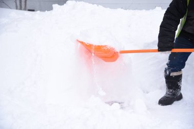 Bir işçi kaldırımlardan kar kaldırır turuncu bir kürekle sürüklenir.