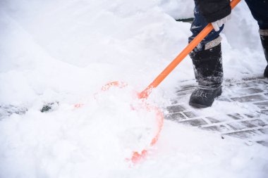 Bir işçi kaldırımlardan kar kaldırır turuncu bir kürekle sürüklenir.