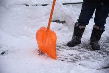 Bir işçi kaldırımlardan kar kaldırır turuncu bir kürekle sürüklenir.