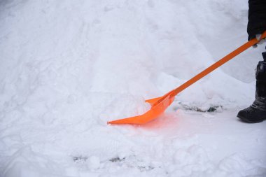 Bir işçi kaldırımlardan kar kaldırır turuncu bir kürekle sürüklenir.
