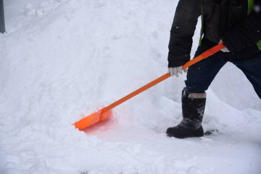 Bir işçi kaldırımlardan kar kaldırır turuncu bir kürekle sürüklenir.