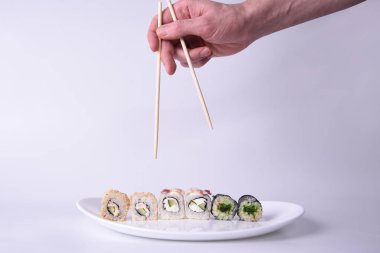 Suşi tatmak için uzanan bir adamın eli bir tabak Japon suşisine pirinç, sebze ve stüdyoda beyaz bir tabakta balık etine yapışır.