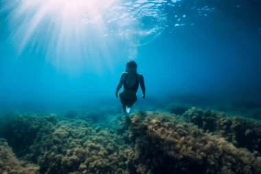 Beyaz yüzgeçli serbest dalgıç kadın inanılmaz güneş ışınlarıyla suyun altında süzülüyor. Okyanusta serbest dalış