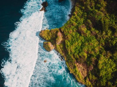 Aerial view of rocky cape with ocean waves in tropical island, Indonesia.