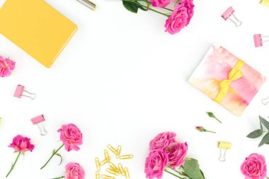 Beyaz arka planda sarı defter, kalem, ataç ve gül çiçekleri olan çerçeve kompozisyonu. Düz yatıyordu.