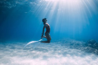 Tropikal okyanusta kumun üzerinde beyaz yüzgeçli kırmızı mayo giyen özgür bir kadın. Sportif kız suyun altına daldı..