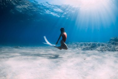 Kırmızı mayo giyen, beyaz yüzgeçli bir kadın tropikal okyanusta kumun üzerinde süzülüyor. Sportif kız suyun altına daldı..
