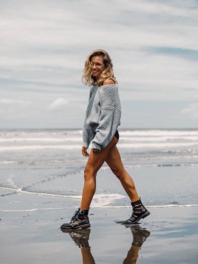 Okyanus sahilinde poz veren çekici, neşeli bir kadın.