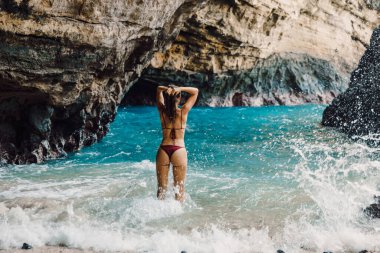 Kumsalda bikinili, zayıf esmer kadın poz veriyor. Tatillerde bronzlaşmış kadın model