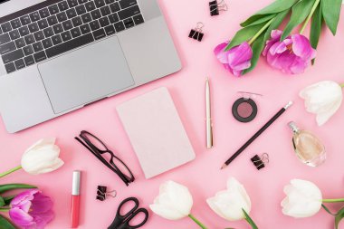 Laptop, lale çiçekleri, not panosu, bardaklar, kalem ve makas pembe üzerine. Düz yatıyordu. Üst Manzara. Serbest Çalışan Konsepti