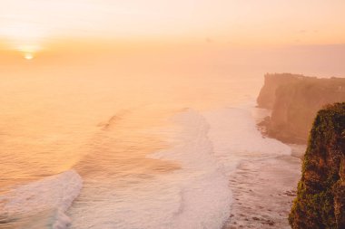Okyanusla, dalgalarla ve Bali 'deki Uluwatu kayalıklarıyla gün batımı