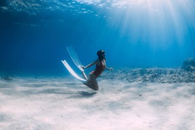 Yüzgeçli bir kadın, tropikal okyanusta kumun üzerinde süzülüyor..