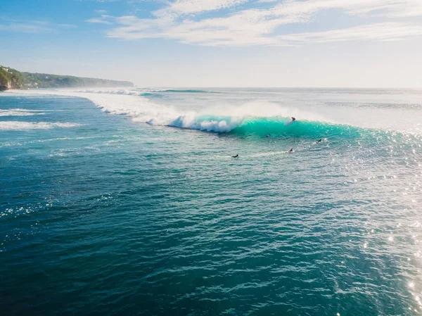 Blue wave with surfers in ocean, drone shot. Aerial view of barrel waves