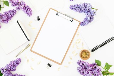 Beyaz arka planda panosu, günlüğü, leylak çiçekleri ve aksesuarları olan ofis kompozisyonu. Düz yatış, üst görünüm.