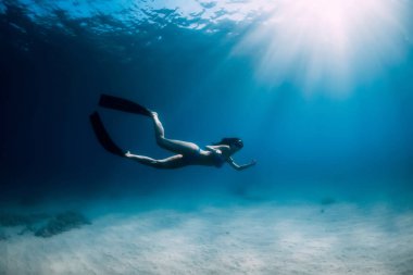 Yüzgeçli serbest dalgıç kadın tropikal okyanusta kumun üzerinde süzülüyor..