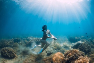 Özgür kadın elinde kumla suyun altında süzülüyor. Şeffaf denizde yüzgeçli serbest dalgıç