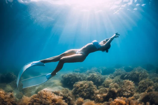 無料のダイバーは白いフィンで砂浜の海を滑空します スリム女性フリーダイバーで青い海 — ストック写真