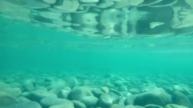 Suyun altında şeffaf okyanus suyu ve altında taşlar olan dalgalar.