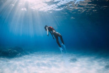 Beyaz yüzgeçli çekici serbest dalgıç süzülüyor ve mavi okyanusta güneş ışığıyla su altında poz veriyor. Sıska kız suyun altına daldı.