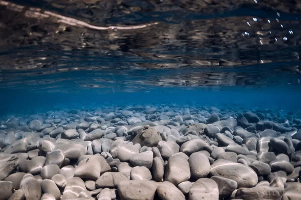 Underwater ocean with stones bottom, reflection and blue water.